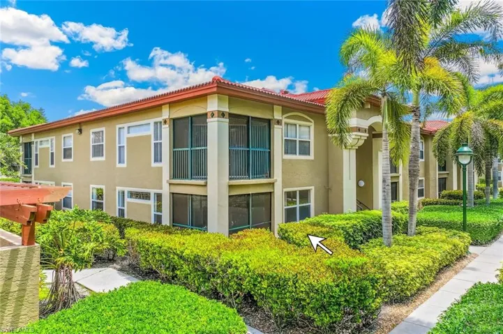View of the rear of the ground floor unit featuring a Mediterranean-style condo building with red tile roof, stucco exterior, multiple screened balconies, mature palm trees, and manicured landscaping