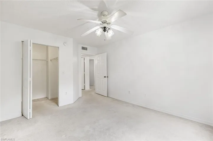 Carpeted interior space featuring a ceiling fan with integrated lighting, bi-fold closet doors, and white painted walls and trim, and large walk-in closet.