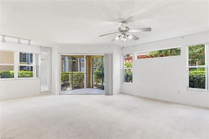 Spacious living area featuring light-colored carpeting and white walls, and slider door to the screened lanai area.