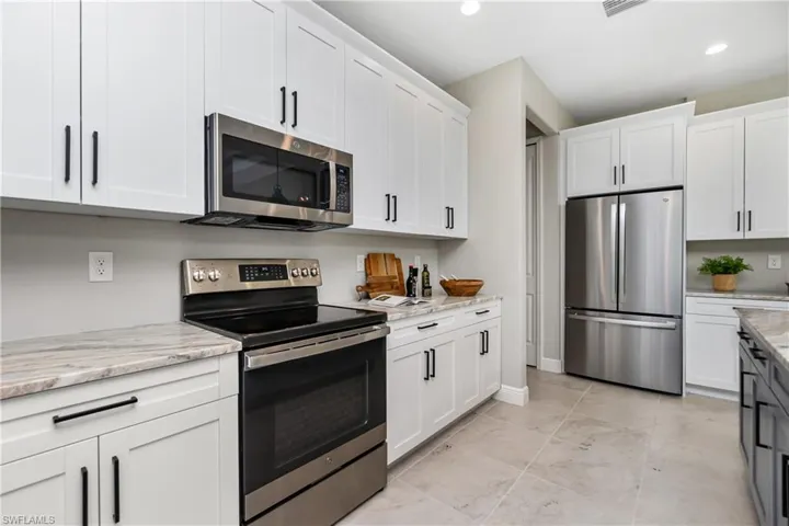 Kitchen with light stone counters, white cabinets, light tile floors, and stainless steel appliances