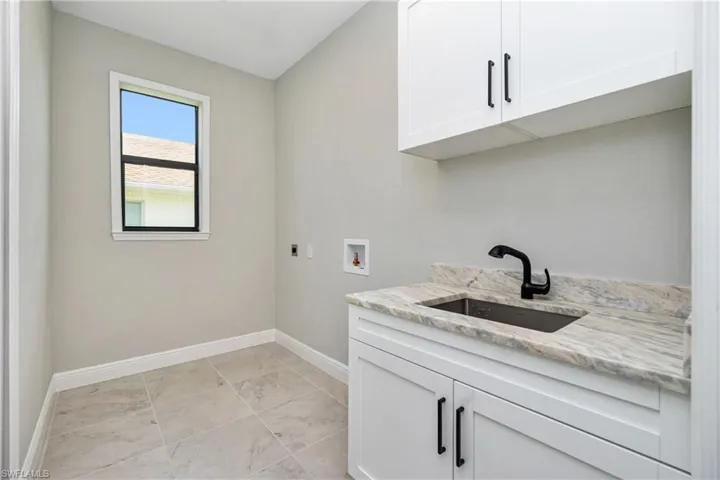 Laundry area with hookup for a washing machine, hookup for an electric dryer, light tile floors, sink, and cabinets