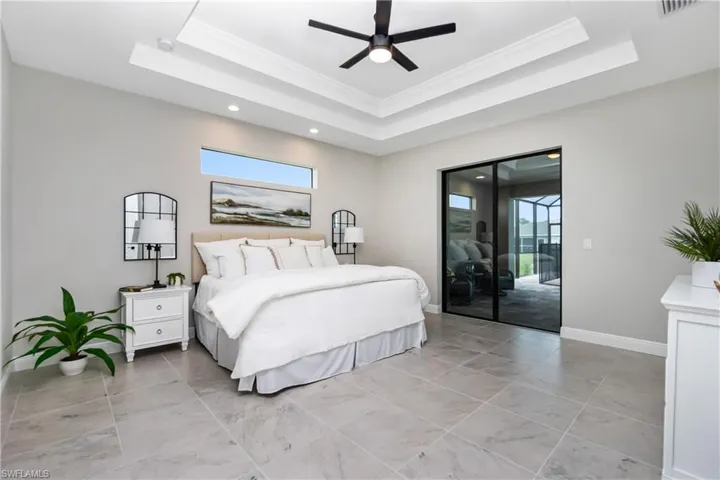 Main bedroom featuring multiple windows, a tray ceiling, ceiling fan, and access to exterior