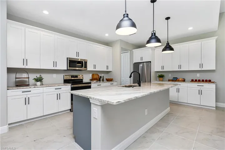 Kitchen with a kitchen island with sink, white cabinets, light tile floors, and stainless steel appliances
