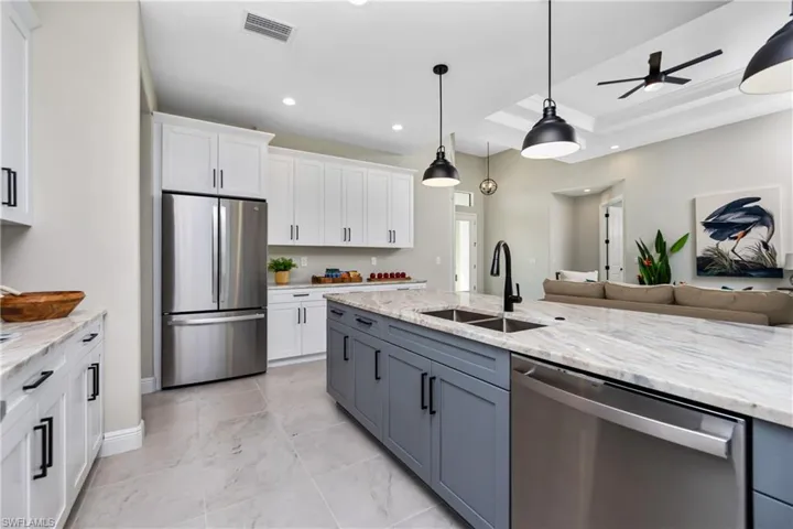 Kitchen with decorative light fixtures, stainless steel appliances, a raised ceiling, white cabinets, and sink