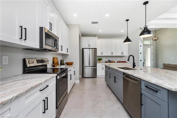 Kitchen with white cabinetry, hanging light fixtures, stainless steel appliances, sink, and light tile floors