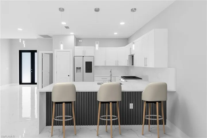 Kitchen with a breakfast bar, white cabinetry, and white refrigerator with ice dispenser