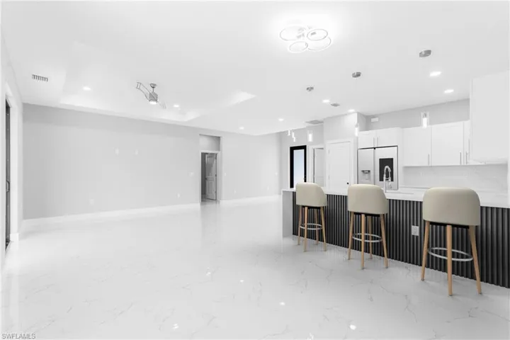 Kitchen with a kitchen breakfast bar, a raised ceiling, white fridge with ice dispenser, decorative light fixtures, and white cabinetry
