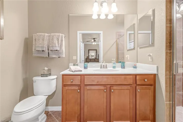 Bathroom featuring tile patterned flooring, an enclosed shower, toilet, vanity, and ceiling fan