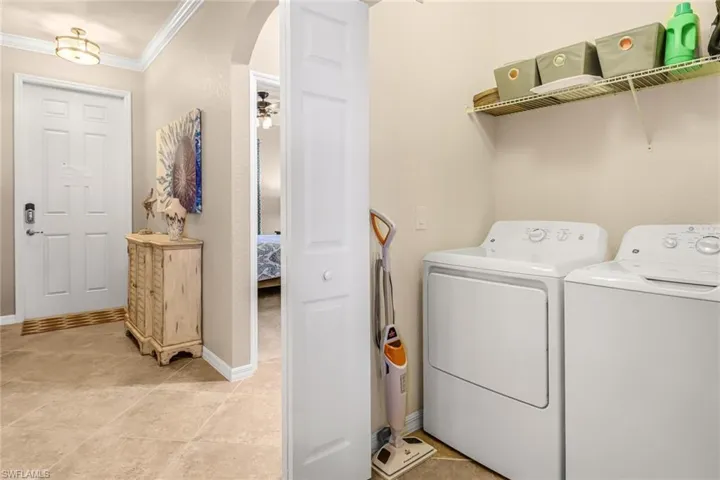 Washroom with washing machine and clothes dryer, ornamental molding, and light tile patterned floors