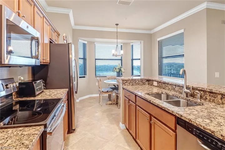 Kitchen with stainless steel appliances, sink, decorative light fixtures, light tile patterned floors, and crown molding