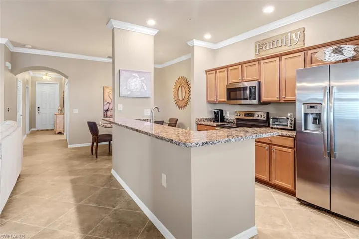 Kitchen featuring light tile patterned flooring, stainless steel appliances, ornamental molding, sink, and light stone countertops