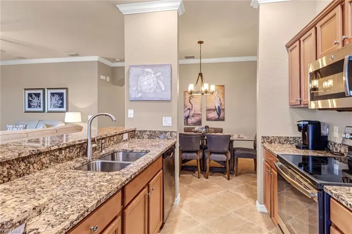 Kitchen featuring crown molding, sink, an inviting chandelier, appliances with stainless steel finishes, and light tile patterned floors