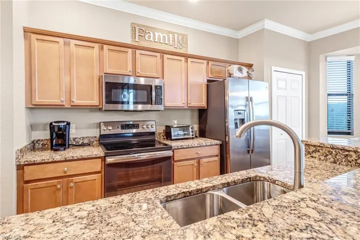 Kitchen with ornamental molding, sink, light stone counters, and stainless steel appliances
