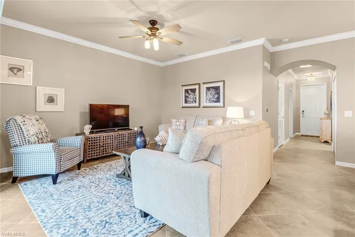 Living room featuring light tile patterned floors, crown molding, and ceiling fan