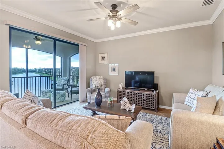 Tiled living room with a water view, ornamental molding, and ceiling fan