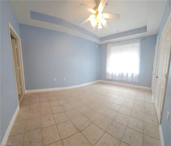 Spare room with ceiling fan, a raised ceiling, and light tile floors