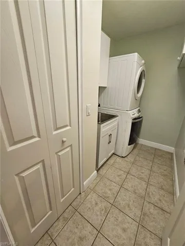 Clothes washing area with stacked washer / dryer, light tile flooring, and cabinets