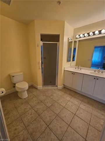 Bathroom with dual vanity, an enclosed shower, tile floors, and toilet