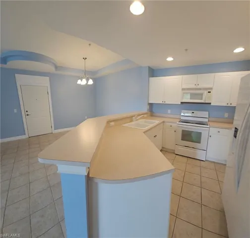Kitchen featuring white appliances, light tile floors, hanging light fixtures, sink, and white cabinets