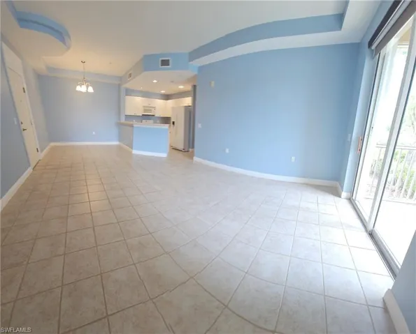Unfurnished living room with a healthy amount of sunlight, a chandelier, light tile flooring, and a tray ceiling