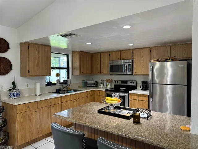 Kitchen featuring stainless steel appliances, a kitchen bar, vaulted ceiling, sink, and light tile patterned flooring