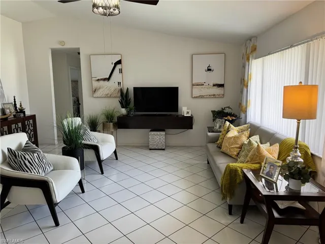 Living room with ceiling fan, light tile patterned floors, and lofted ceiling