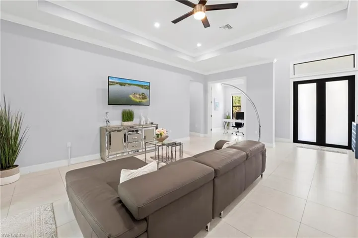 Spacious living area featuring light-colored tile flooring, a ceiling fan with integrated lighting, and a tray ceiling