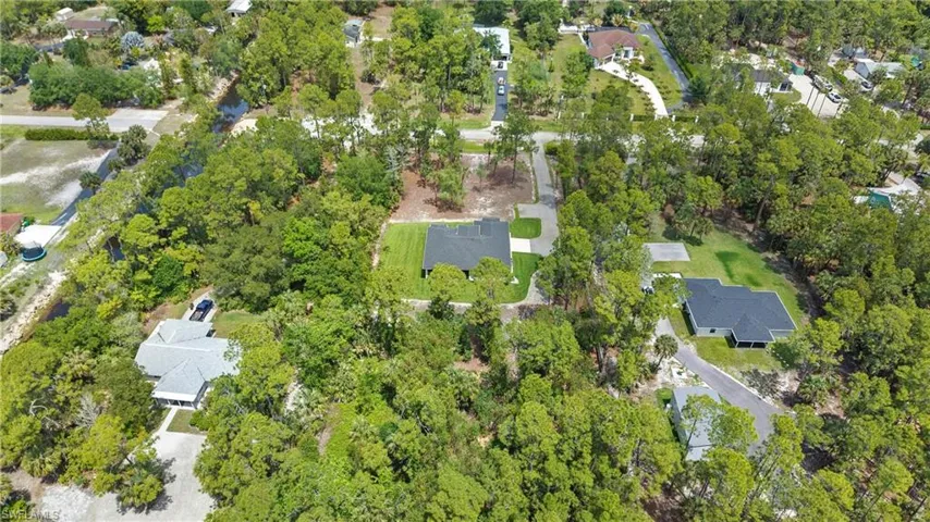 This property offers an expansive lot with lush green trees and a well-maintained lawn, featuring a light-colored exterior and a dark roof