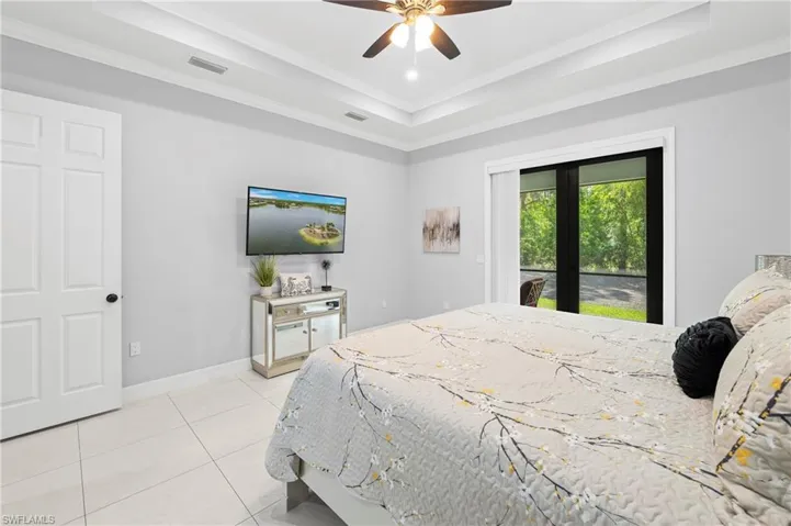 This bedroom features a tray ceiling, tiled flooring, and a ceiling fan