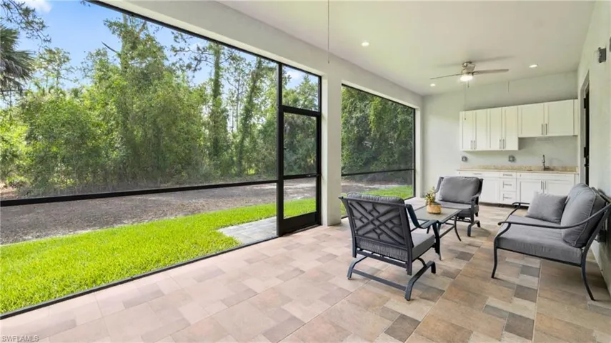 Expansive screened patio featuring textured tile flooring, recessed lighting, and an outdoor kitchen with white cabinetry and a sink, perfect for entertaining