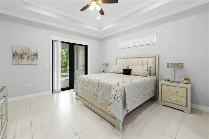 Spacious sleeping area featuring light-colored tile flooring, a tray ceiling, and a ceiling fan