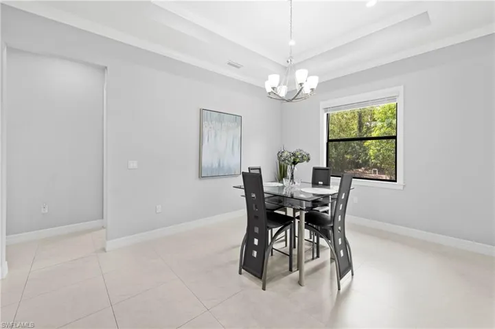 Dining area featuring light-colored tiled flooring, a tray ceiling, and a window providing a view of greenery