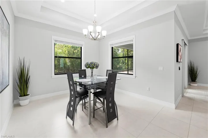 The property features a dining area with light-colored tile flooring, multiple windows providing views of exterior greenery, and a chandelier