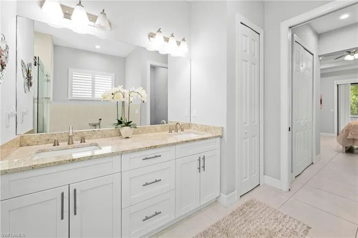 The bathroom features a double vanity with light-colored granite countertops, white cabinetry, and brushed nickel hardware