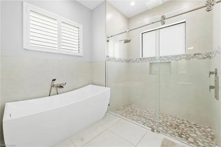 The bathroom features a freestanding soaking tub with a floor-mounted faucet, a walk-in shower with a glass enclosure and a rain showerhead, and tiled walls and flooring