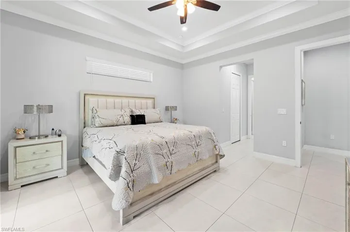 This bedroom features a tray ceiling with a ceiling fan, light-toned tiled flooring, and neutral wall paint