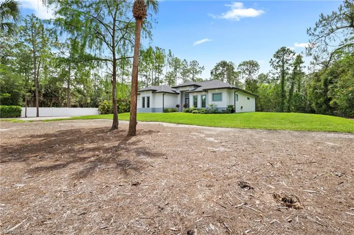 The property features a contemporary style exterior with a light-colored facade and dark roof, set against a backdrop of mature trees and a clear blue sky