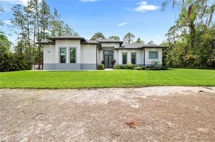 The property features a modern exterior with a white and gray facade, a dark roof, and a well-maintained green lawn