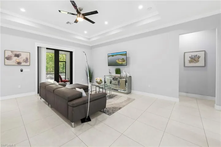 Spacious living area featuring large format tile flooring, a tray ceiling with recessed lighting and a ceiling fan, and access to an outdoor space through black framed French doors