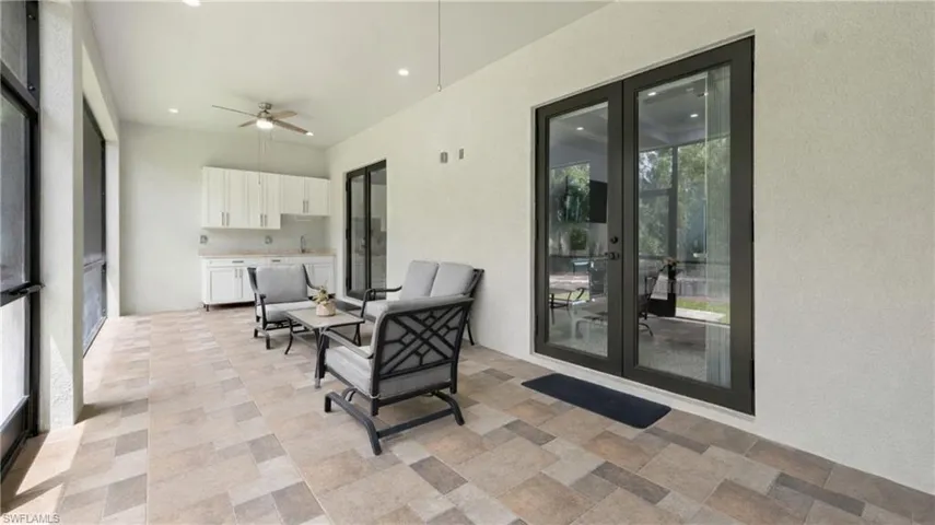 The property features an expansive covered patio with large format tile flooring, a ceiling fan, and a wet bar with white cabinetry and a light-colored countertop