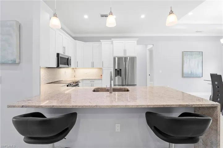 Modern kitchen featuring white cabinetry, stainless steel appliances, and a light-colored granite countertop with an integrated sink