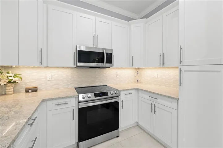 The kitchen features white cabinetry, granite countertops, a tile backsplash, and stainless steel appliances including a microwave and range