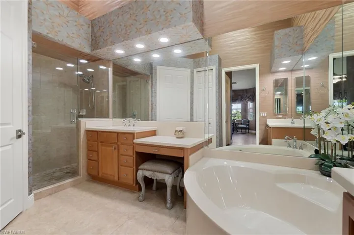 Spacious bathroom featuring a built-in corner soaking tub, a glass-enclosed shower, dual vanity with wood cabinetry, and extensive mirror coverage