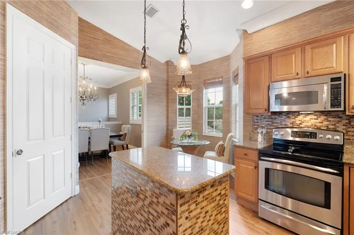 Kitchen featuring a stone countertop island with mosaic tile surround, stainless steel appliances, wood-finish flooring, and pendant lighting