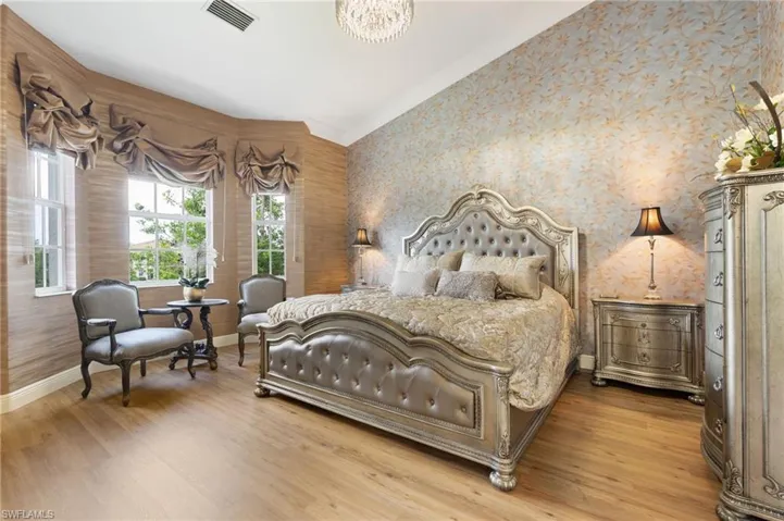 Spacious room featuring wood-finish flooring, multiple windows with custom window treatments, and patterned wall coverings