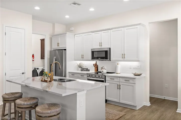 Kitchen featuring light wood-style floors, a center island with sink, a kitchen breakfast bar, backsplash, and recessed lighting