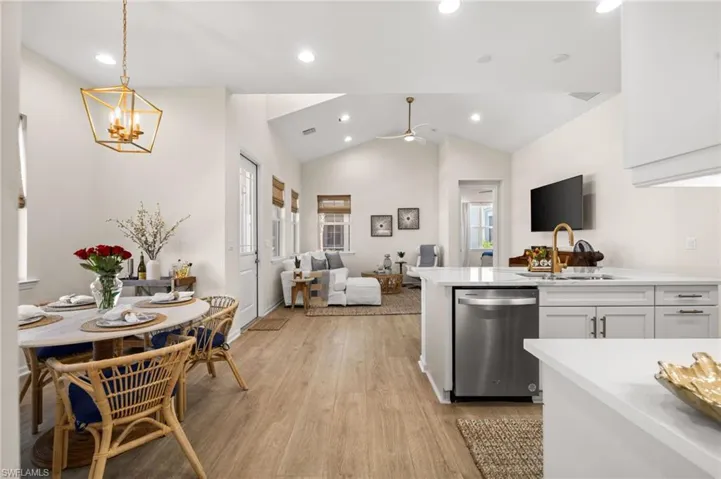 Kitchen with white cabinets, stainless steel dishwasher, lofted ceiling, light wood finished floors, and pendant lighting