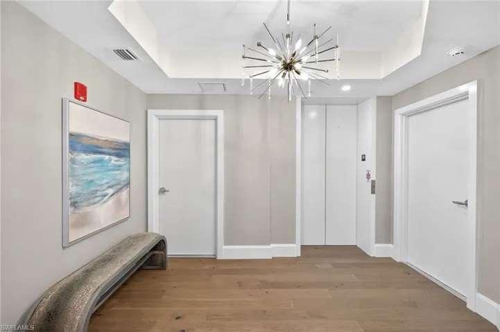 Large foyer entrance off elevator is welcoming with light wood floors and stylish chandelier