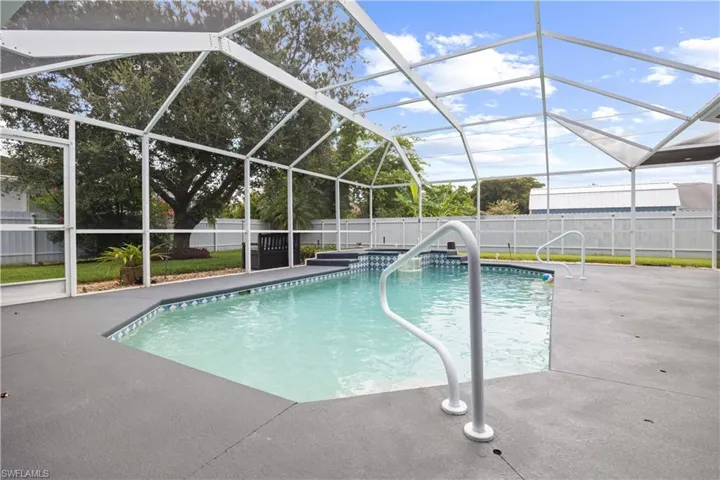 Screen-enclosed swimming pool with integrated spa featuring white handrails, a geometric shape, and decorative blue mosaic tile