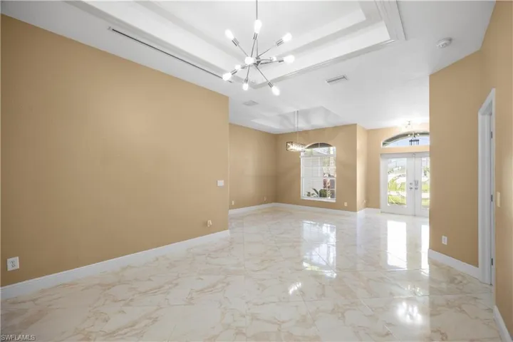 Spacious interior featuring large format marble-look tile flooring, a tray ceiling with a contemporary chandelier, arched windows, and double French doors